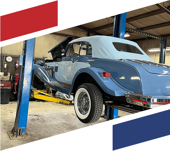 A blue vintage car suspended in an auto repair shop